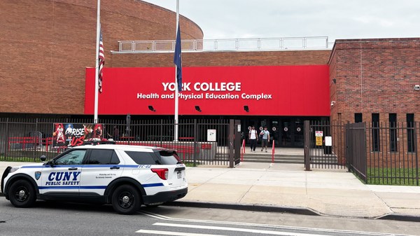 A view of the York College Health and Physical Education Complex building, featuring a red facade, with a police vehicle parked in the foreground.
