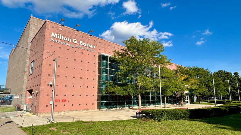 The exterior of the Milton G. Bassin Performing Arts Center at York College, featuring red brick and large glass windows under a blue sky.