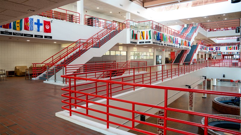 A bright, multi-level interior view showing red staircases and railings in a modern institutional building.