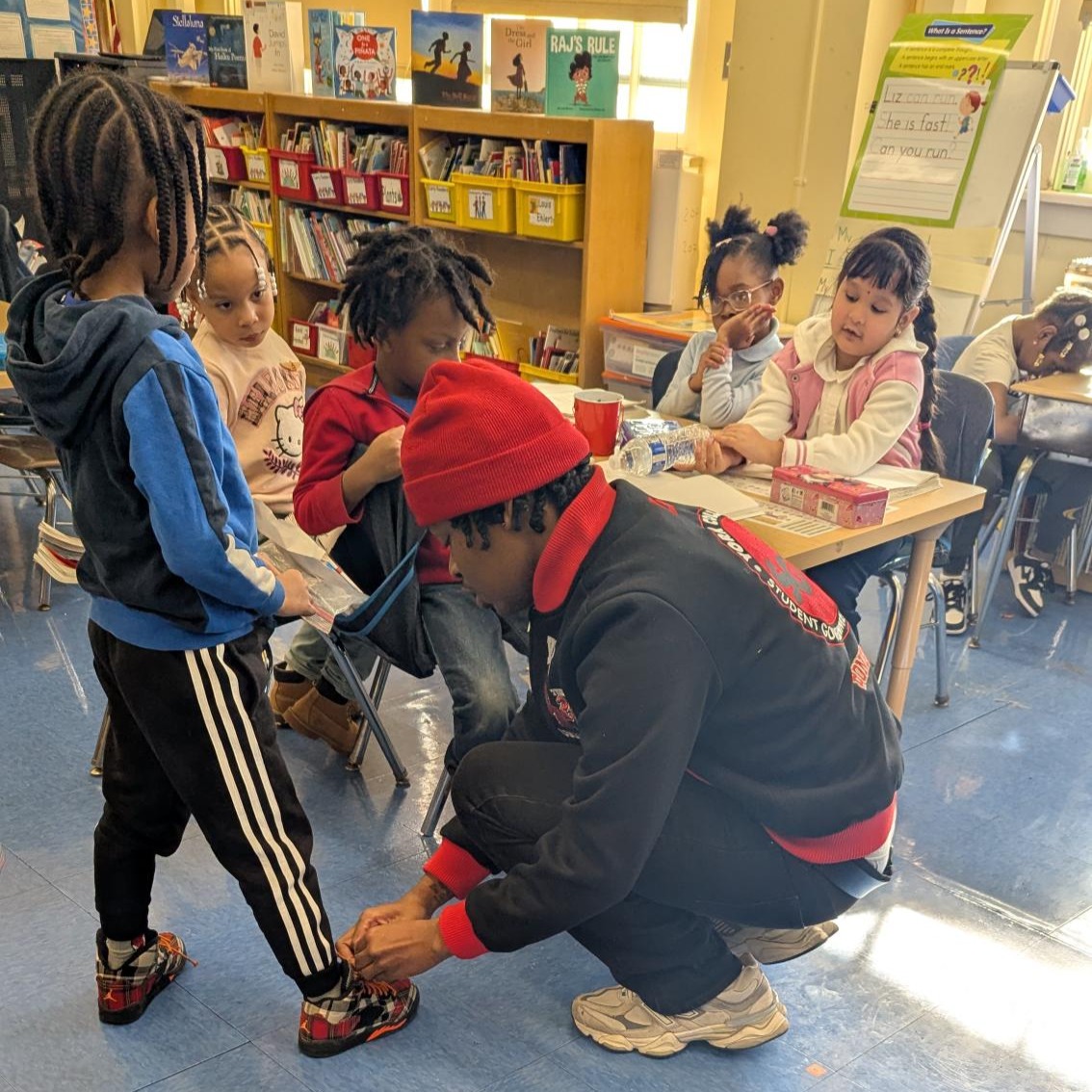 Project Serve volunteer helps a child with his shoelace during a group visit to an elementary school visit.
